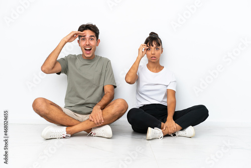 Young mixed race couple sitting on the floor isolated on white background intending to realizes the solution while lifting a finger up