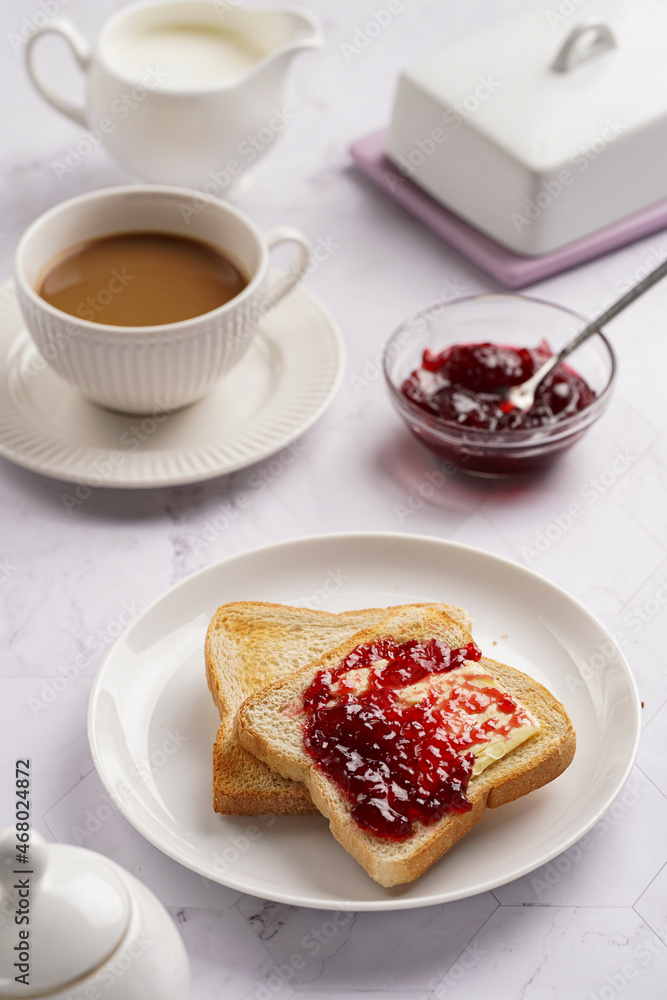sweet breakfast - toast bread with butter and cherry jam on a white plate, cup of cappuccino sweet breakfast - toast bread with butter and cherry jam on a white plate, cup of cappuccino