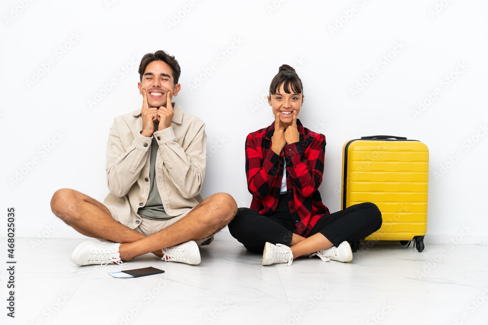 Obraz premium Young mixed race travelers couple sitting on the floor isolated on white background smiling with a happy and pleasant expression