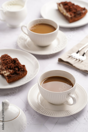 sweet breakfast - two white porcelain cups with coffee drink cappuccino with milk on a white saucer, piece of brown cake