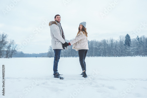 Young happy couple walk in winter park holding hands. Family of man and woman spend time together during winter holidays.