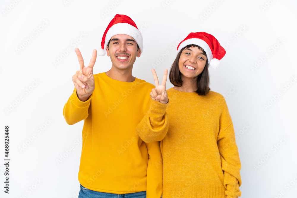 Young mixed race couple celebrating Christmas isolated on white background smiling and showing victory sign Young mixed race couple celebrating Christmas isolated on white background smiling and showing victory sign
