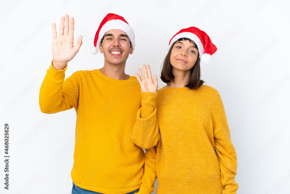 Young mixed race couple celebrating Christmas isolated on white background saluting with hand with happy expression Young mixed race couple celebrating Christmas isolated on white background saluting with hand with happy expression