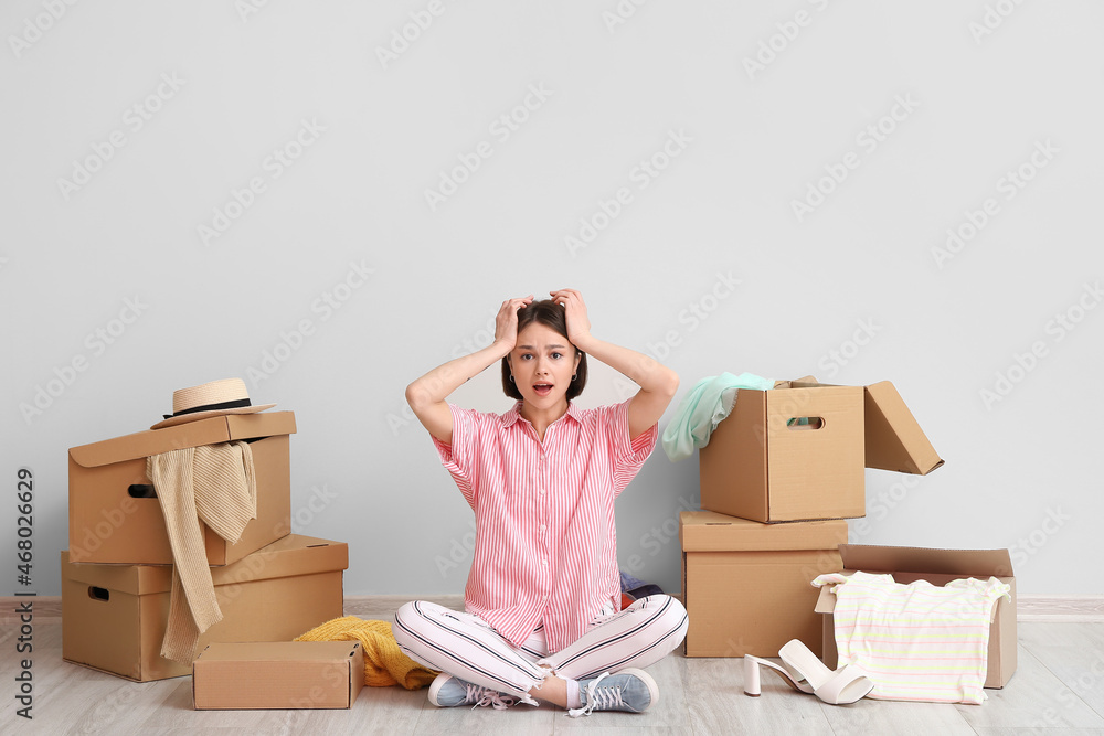 Stressed young woman with wardrobe boxes and things near light wall - obrazy, fototapety, plakaty 