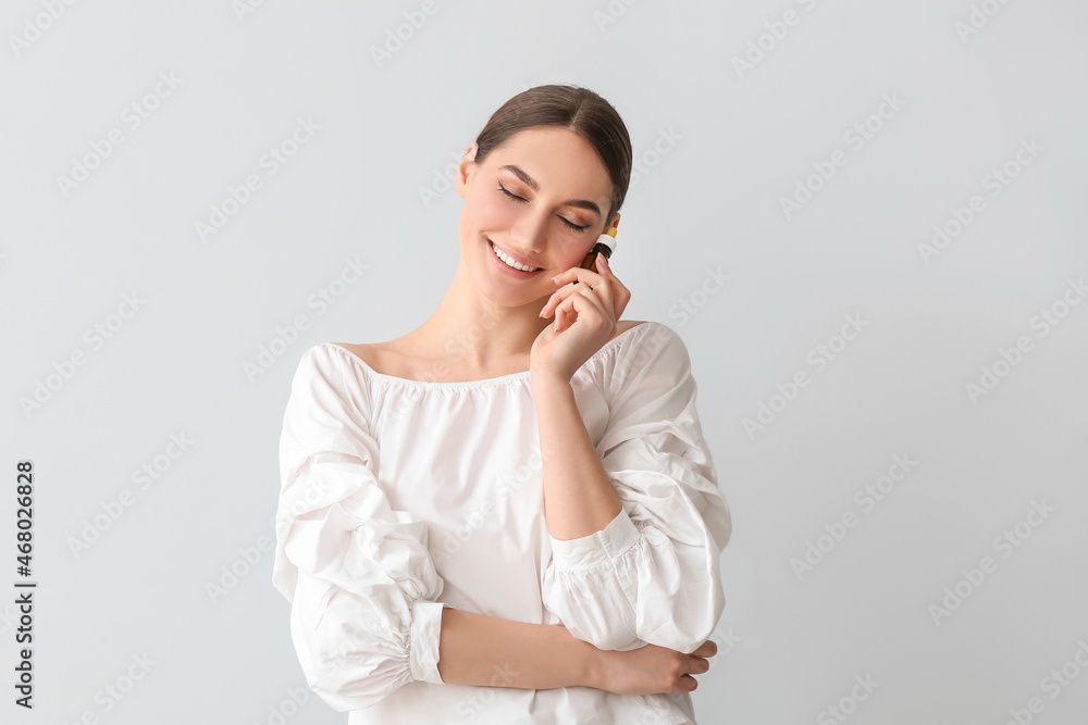 Smiling woman with closed eyes holding bottle of essential oil on light background Smiling woman with closed eyes holding bottle of essential oil on light background
