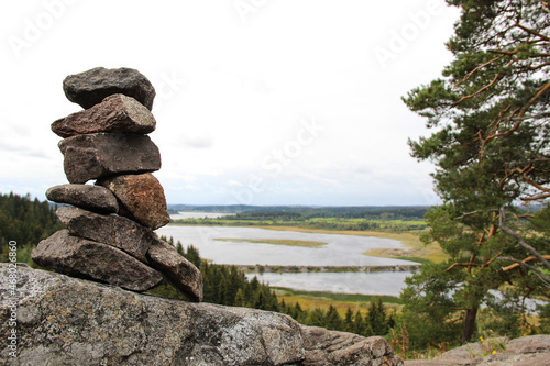 Pyramid made by stones. Beautiful landscape. Stone tower and river, trees in the background. Rocks on the pine forest. Stone pile was made by tourist. Concept of balance, harmony and vacation.