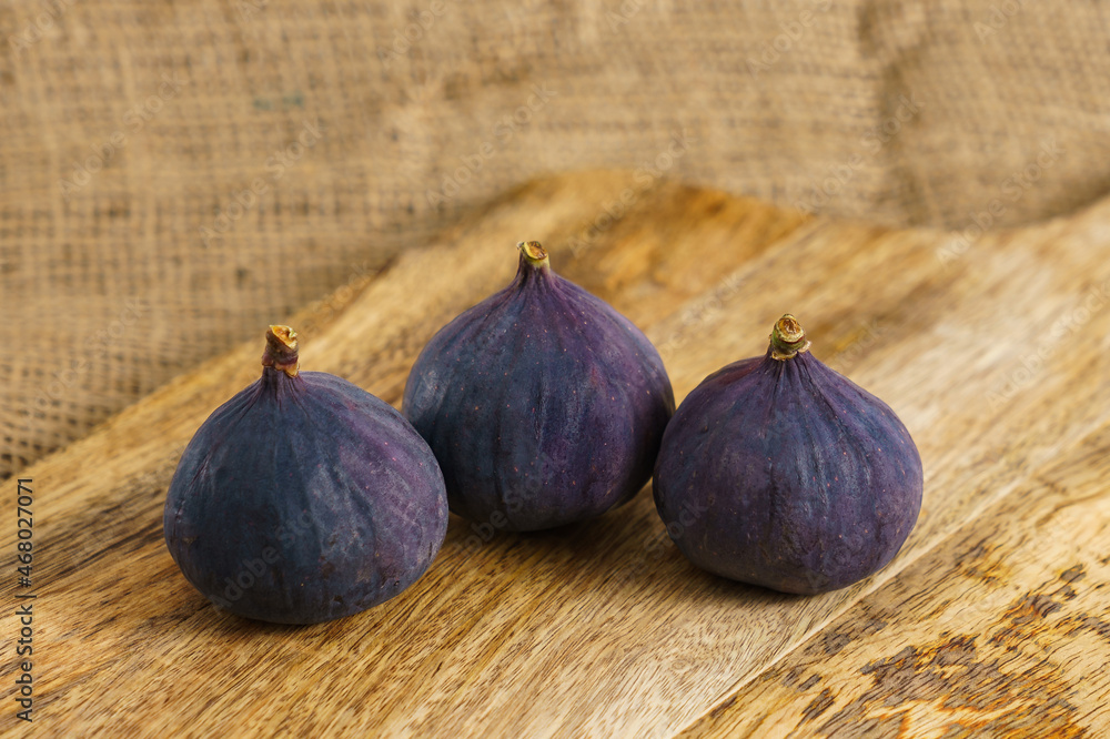 Fototapeta premium Three fig fruits on old wooden chopping board.