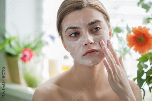 Beautiful young girl cleansing face with cosmetic facial skincare foam, gel or soap.