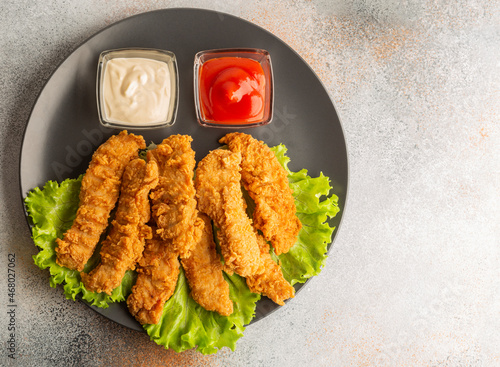 Fotografie Breaded chicken strips with two kinds of sauces on gray plate
