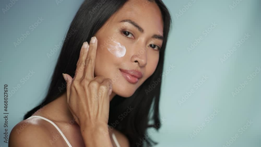 Female Beauty Portrait. Beautiful Asian Brunette Woman Touching Natural, Healthy Skin, Using Facial Moisturizer, Applying Face Cream. Wellness and Skincare Concept on Isolated Background. Female Beauty Portrait. Beautiful Asian Brunette Woman Touching Natural, Healthy Skin, Using Facial Moisturizer, Applying Face Cream. Wellness and Skincare Concept on Isolated Background.