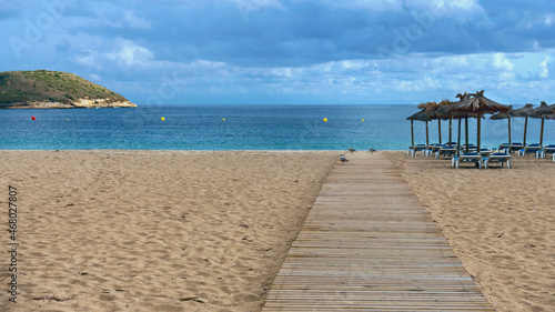 wooden walkway on a sandy beach against the backdrop of the sea  straw umbrellas and plastic sunbeds
