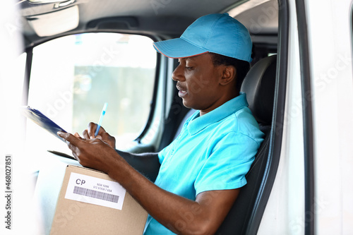 African-American courier of delivery company sitting in car