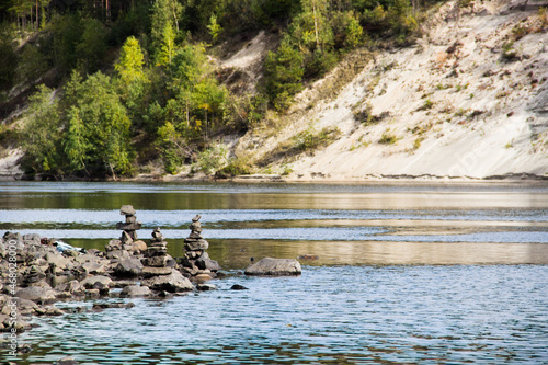 Beautiful landscape. Pyramid made by stones. Stone tower and river, forest in the background. Rocks on the pine forest. Stone pile was made by tourist. Concept of balance, harmony and vacation.