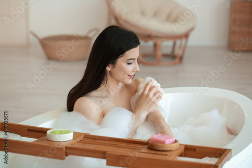 Relaxed young woman taking bath with loofah at home photo