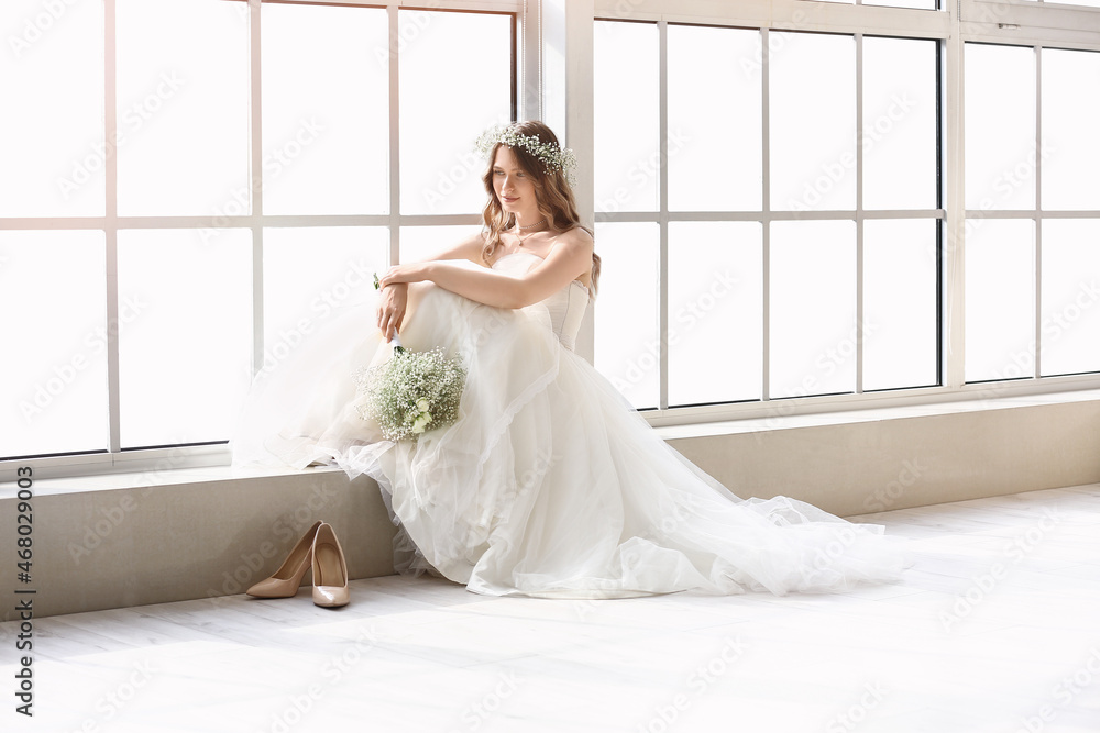 Beautiful bride with bouquet of flowers sitting on window sill