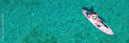Woman paddle on sup board doing water sport during summer holidays. Concept of active tourism and travel. Aerial wide banner © Leonid