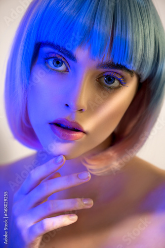 Beautiful young woman in pink and blue wig with clean perfect skin and makeup in neon studio light with light and shadows in her skin. Selective focus. Portrait of beauty model with long eyelashes,