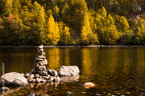 Beautiful landscape. Pyramid made by stones. Stone tower and river, forest in the background. Rocks on the pine forest. Stone pile was made by tourist. Concept of balance, harmony and vacation.