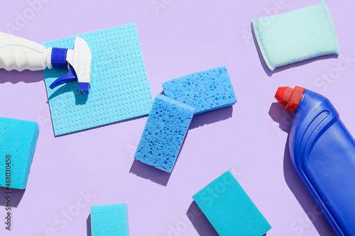 Blue cleaning sponges and bottles of detergent on color background