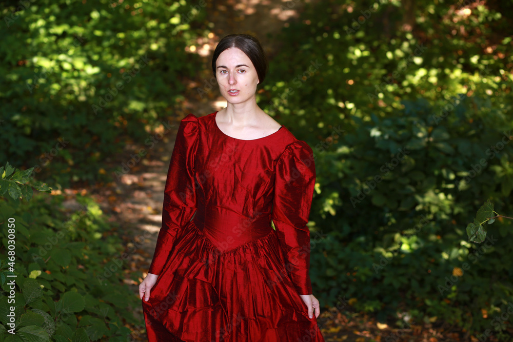 Woman in red dress standing on a path in the forest Woman in red dress standing on a path in the forest