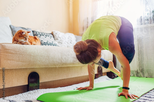 Home yoga workout during coronavirus lockdown. Kakasana crow pose. Woman training using mat by cat. photo