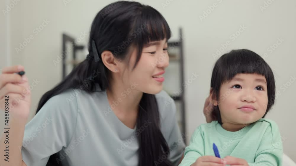 Mom kissing son and teaching how to painting with crayon color on book or doing homework. Happy asian boy painting with crayon with his mother in living room at home. Family having fun concept. Mom kissing son and teaching how to painting with crayon color on book or doing homework. Happy asian boy painting with crayon with his mother in living room at home. Family having fun concept.
