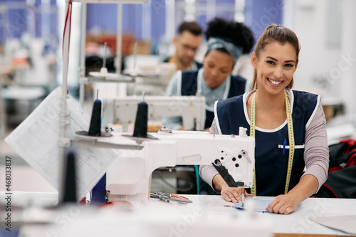 Young happy seamstress works at production line in factory and looks at camera. photo