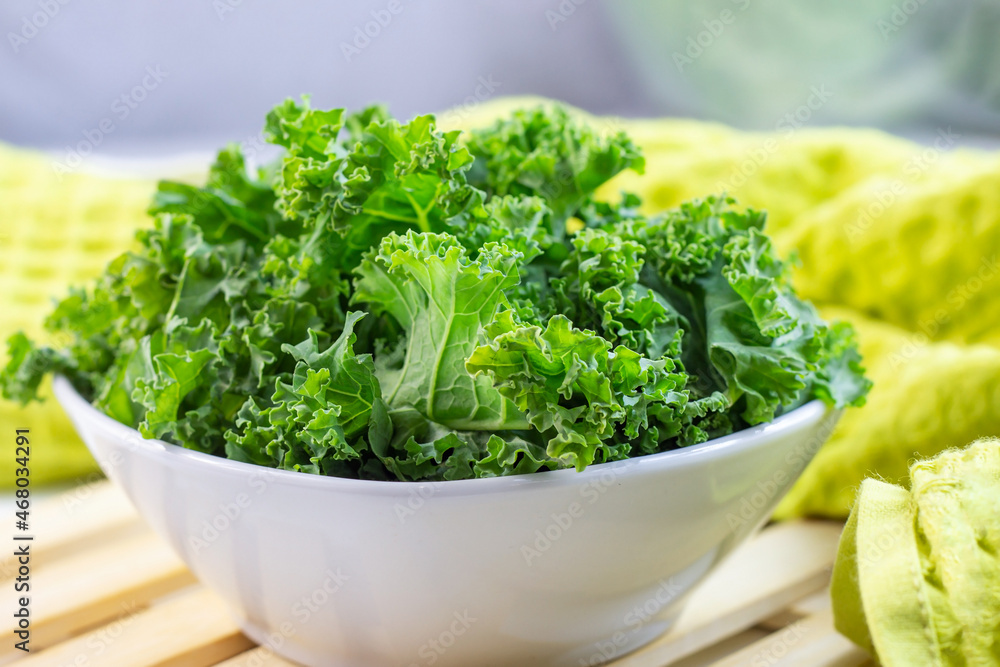 Fresh green curly cabbage or kale salad leaves cut in the bowl on light background on the table in the kitchen. Fresh green curly cabbage or kale salad leaves cut in the bowl on light background on the table in the kitchen.