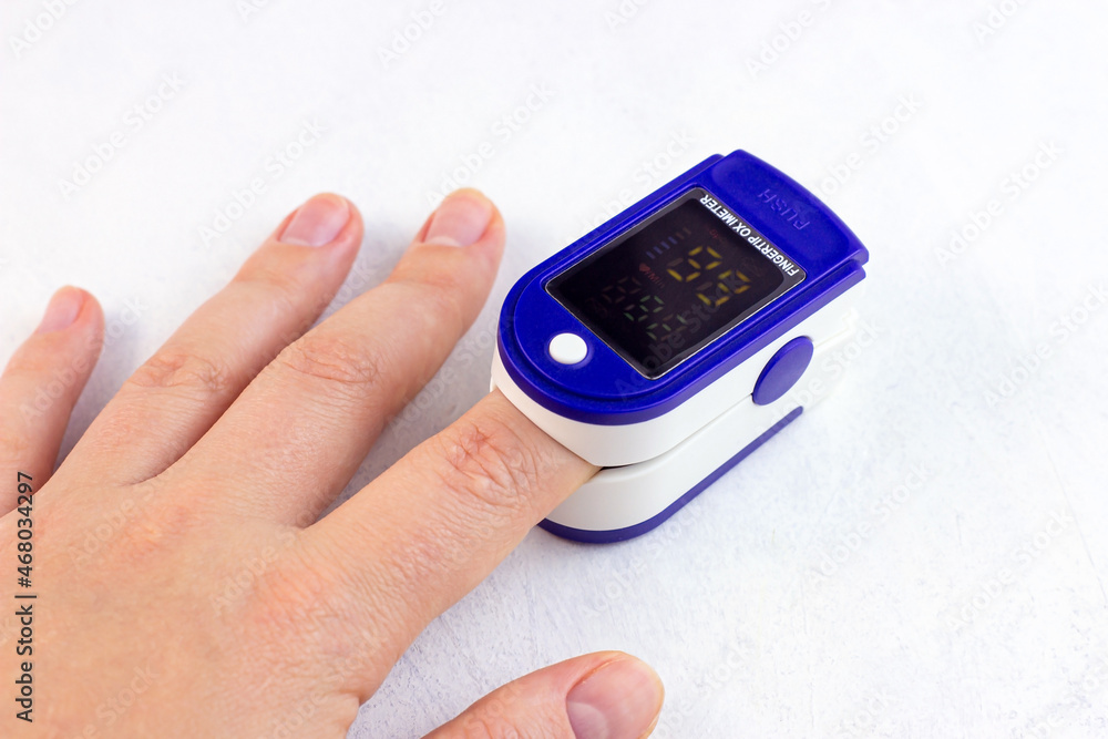 Woman hand with medical fingertip pulse oximeter tool for oxygen saturation check during covid virus desease. SpO2 monitoring and heart rate measurement instrument on light background. Woman hand with medical fingertip pulse oximeter tool for oxygen saturation check during covid virus desease. SpO2 monitoring and heart rate measurement instrument on light background.