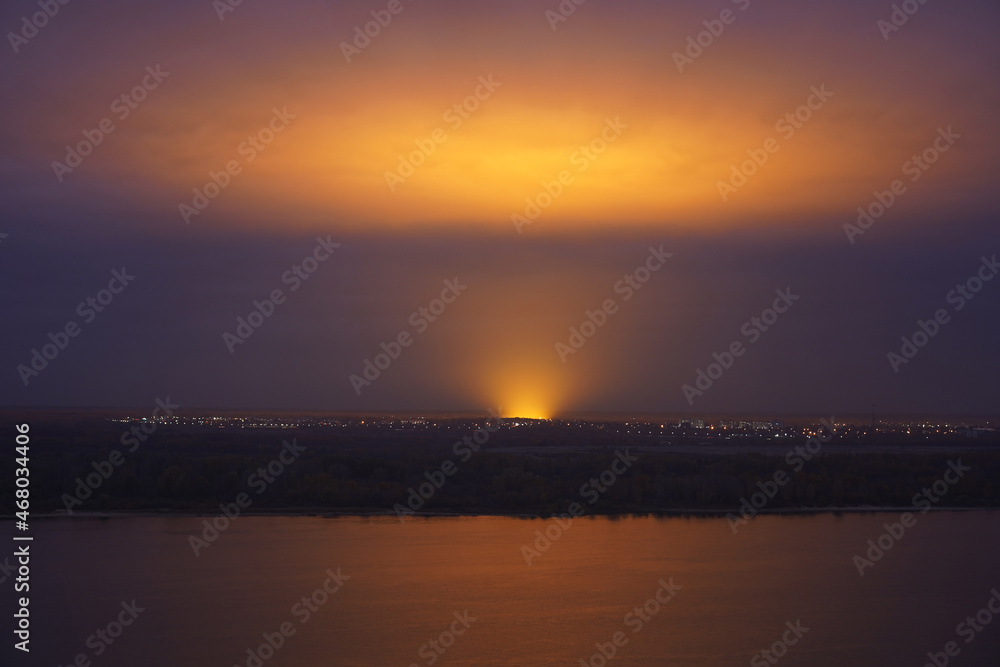 Beautiful evening landscape, yellow glow from powerful lamps at the stadium, concert reflected from the clouds