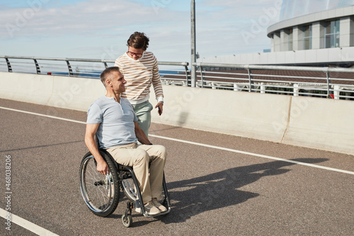 Full length portrait of mature couple with man in wheelchair chatting outdoors and enjoying city life, copy space photo