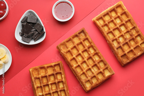 Delicious Belgian waffles with chocolate, jam and banana on color background