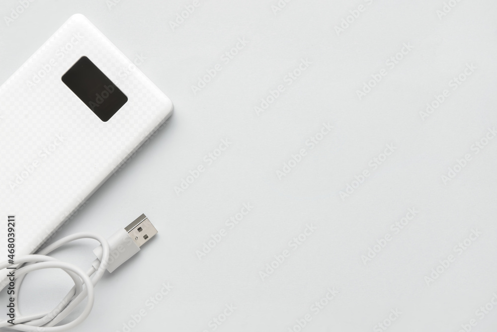 Modern power bank and USB cable on light background, closeup Modern power bank and USB cable on light background, closeup