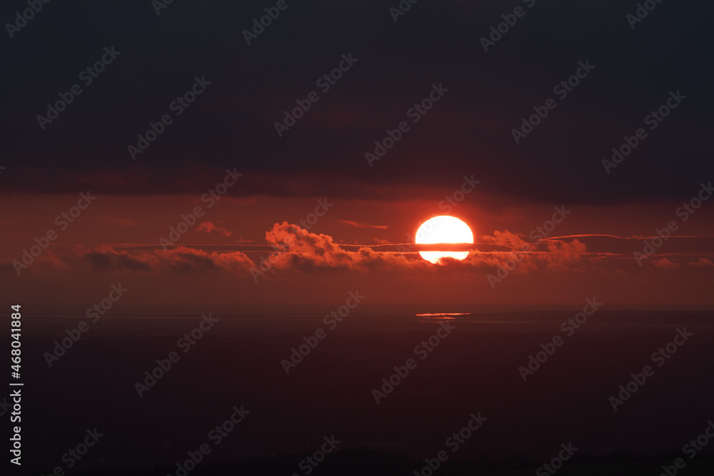 Sunset against dark moody orange sky, with the sun's disc breaking through clouds, with large areas of blank space for copy or text