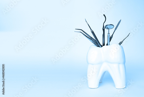 Dental professional steel tools in tooth shaped holder on blue background. Set of metal medical equipment tools for teeth dental care. sickle probe, dental explorer, mirror, burnisher, forceps