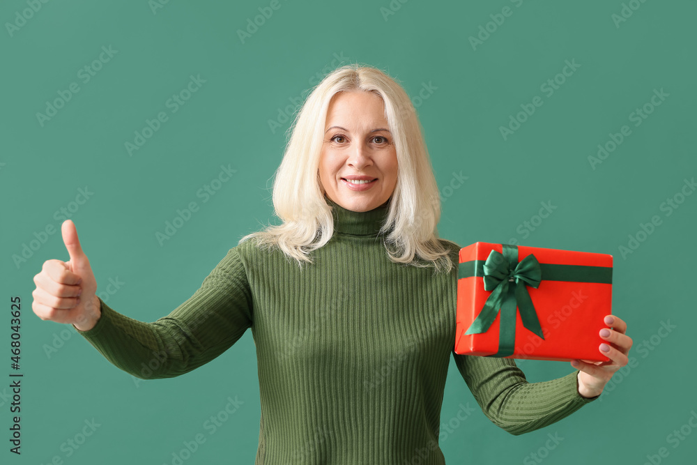 Mature woman with Christmas gift box showing thumb-up on color background Mature woman with Christmas gift box showing thumb-up on color background