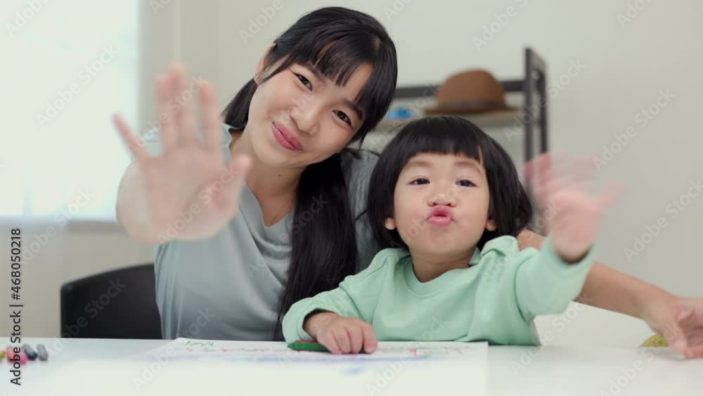 Happy moment asian mother and little boy say hi or bye bye to camera while painting with crayon at home. Family having fun in the house. Mom teaching son homework. Happy moment asian mother and little boy say hi or bye bye to camera while painting with crayon at home. Family having fun in the house. Mom teaching son homework.