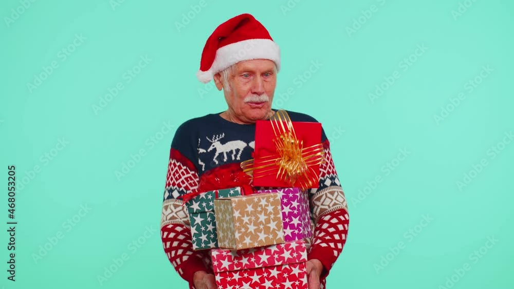 Senior grandfather man in Christmas sweater looking surprised at mount of boxes hands, excited by so many holiday gifts lot of presents on blue studio background. Happy New Year shopping sale holidays Senior grandfather man in Christmas sweater looking surprised at mount of boxes hands, excited by so many holiday gifts lot of presents on blue studio background. Happy New Year shopping sale holidays