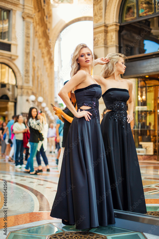 Attractive young blonde girl walking in long black evening dress outdoors