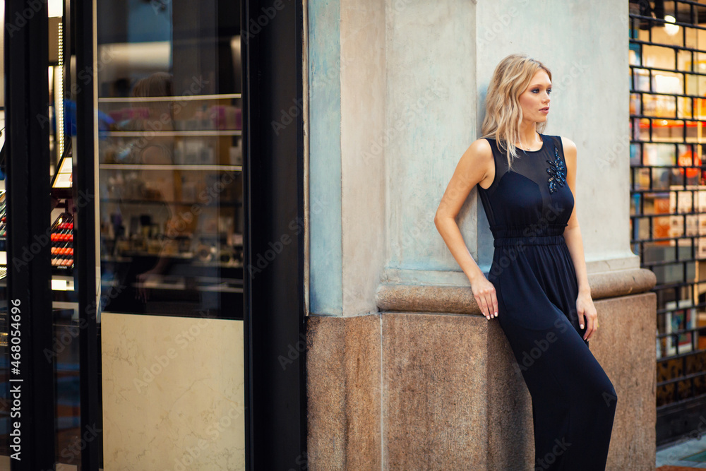 Fototapeta premium Attractive young blonde girl walking in long black suit outdoors