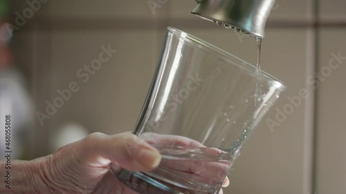 Low water and pressure levels evident by a slow trickle from this kitchen faucet into the glass this woman is holding.