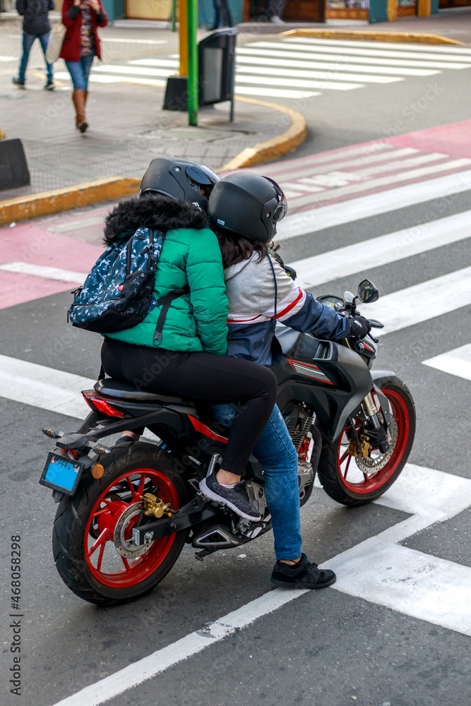Two women riding a motorcycle and waiting at traffic light on a city street during daytime
