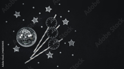 Paper clock on straws, silvery stars, disco ball and snow ball on the left on black