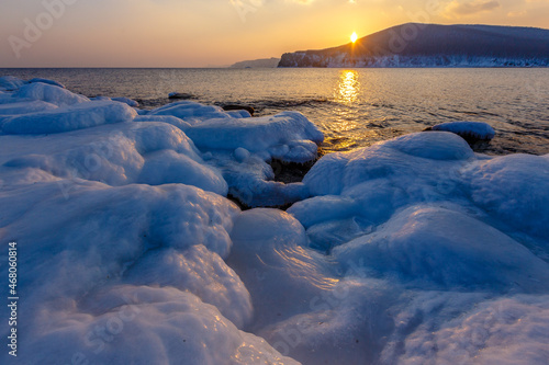 Colorful sunset on the snowy coast of the Sea of Japan. The Sonce goes over the snowy hills against the backdrop of the calm sea. Sikhote-Alin Biosphere Reserve in the Primorsky Territory.