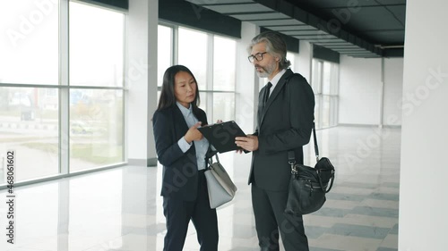 Asian businesswoman talking to partner studying papers standing indoors in modern glass walls building duscussing real estate deal. photo