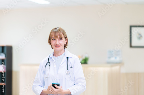 Caucasian senior woman doctor with stethoscope standing in hospital photo