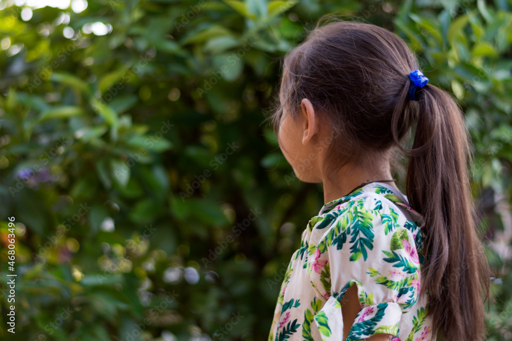 little 7-year-old girl with brown hair and flat skin facing the trees