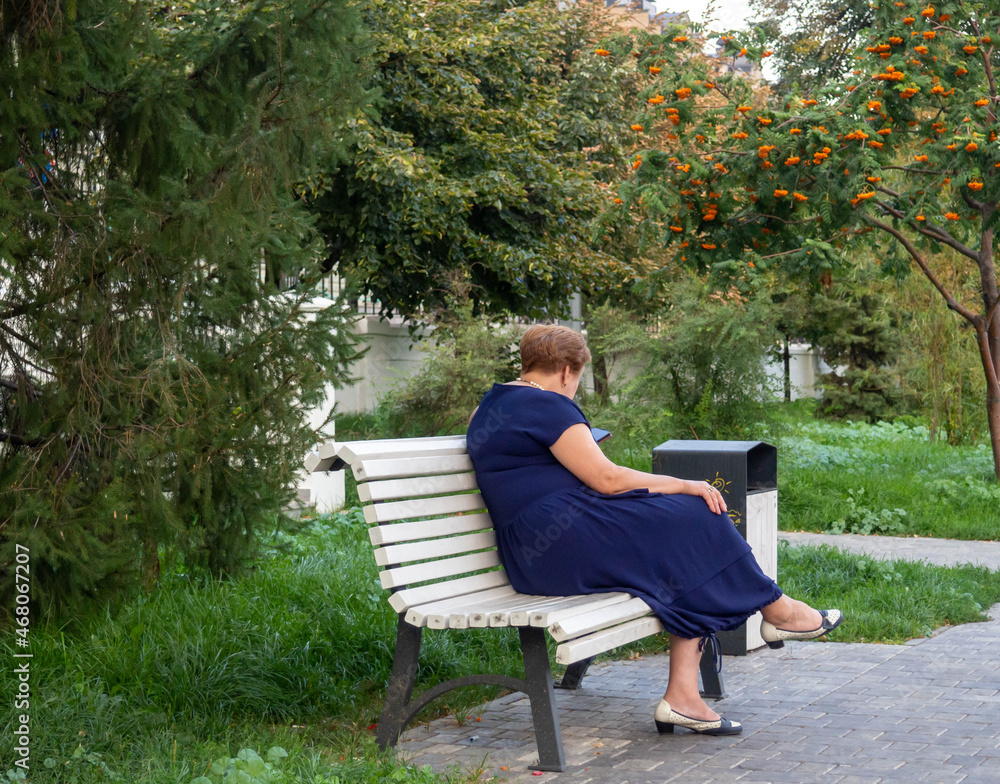 Fototapeta premium A woman is sitting with a phone on a park bench.