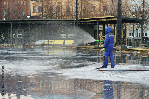 City preparing for winter: worker in uniform hold water hose filling area for ice rink, outdoor activities in urban, winter sport games and hockey competition. Wintertime season preparation concept