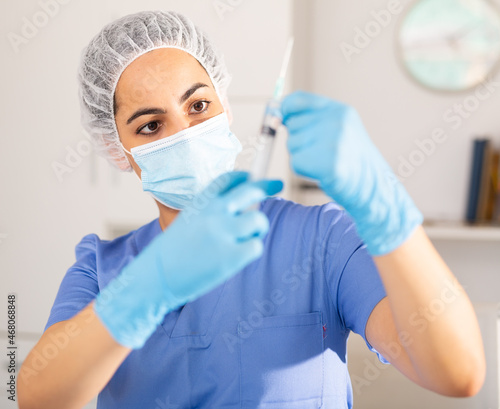 Girl nurse in mask holding syringe for injection in clinic